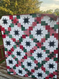 a large quilt on a wooden bench in front of some trees and grass, with one block missing