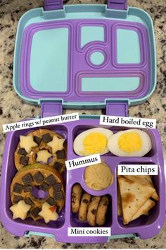 a purple lunch box with food in it and instructions to make an egg, crackers, hummus, cookies