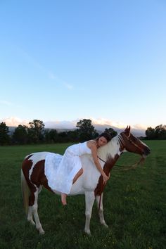 a woman in white dress sitting on top of a brown and white horse's back