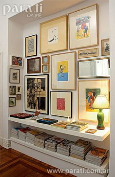 a room filled with lots of framed pictures on the wall next to a lamp and bookshelf