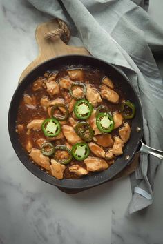 a skillet filled with chicken and peppers on top of a wooden cutting board next to a gray towel