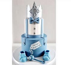 a blue and white cake with baby shoes on it's bottom tier, topped with a crown