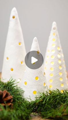 three white christmas trees sitting on top of a wooden table next to pineconi