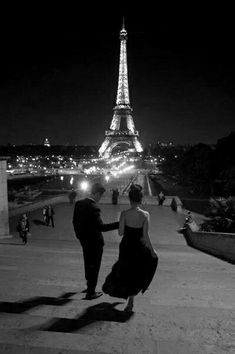 black and white photograph of two people in front of the eiffel tower at night