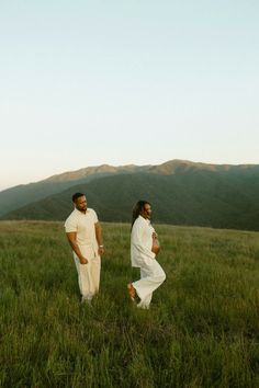 two people standing in the middle of a field with mountains in the backgroud