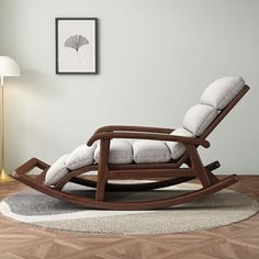 a rocking chair in a living room with a lamp on the floor and pictures above it