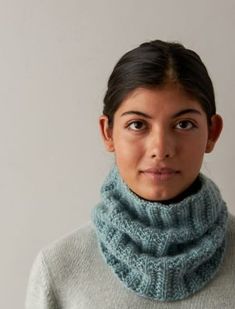 a woman wearing a blue knitted cowl neck scarf and looking at the camera