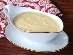 a white bowl filled with soup sitting on top of a saucer next to a red and white napkin