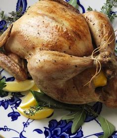 a whole chicken on a plate with lemons and herbs