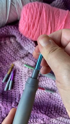 a person holding a pen in their left hand and crochet hooks on the other