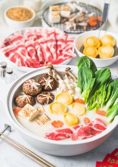 various foods are displayed in bowls on a table with chopsticks and utensils