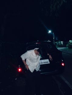 a person leaning on the back of a car at night