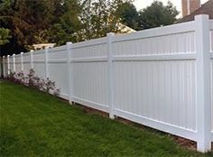 a white picket fence in front of a house with grass and flowers on the side