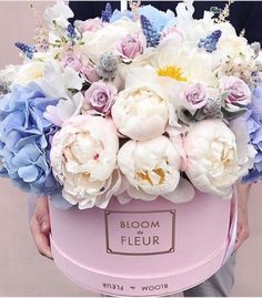 a person holding a pink flower box with white and blue flowers