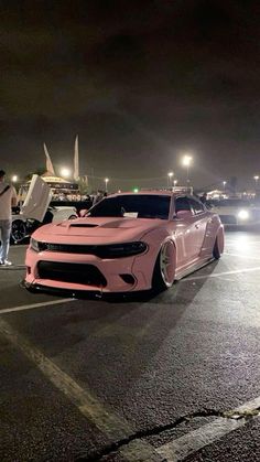 two pink cars parked in a parking lot at night with people standing around the car