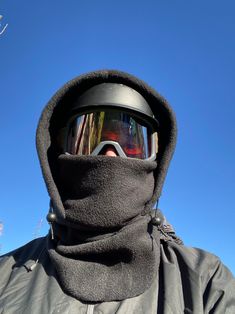 a man wearing ski goggles and a black jacket is standing in front of a blue sky