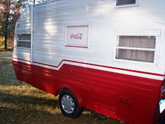 a red and white camper parked in the grass with coca cola on it's side