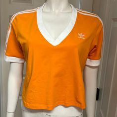 Great Cropped Length Athletic/Athleisure Shirt By Adidas! In A Vibrant Orange With White Stripes, Embroidered Logo, And Cuffed Sleeves, This Top Has Sporty Style! Size 1x (Armpit To Armpit: 20.5” Length: 19”) New With Tags! Summer Sports Tops With Three Stripes Branding, Summer Sports Tops With Three Stripes, Orange Sporty Tops For Sports, Sporty Orange Tops For Sports, Adidas Cotton Sportswear Tops, Adidas Relaxed Fit Athleisure Top, Casual Workout Tops In Orange, Orange Cotton Workout Top, Casual Workout Orange Tops