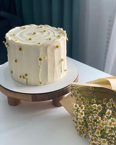 a white cake sitting on top of a table next to a piece of paper and flowers