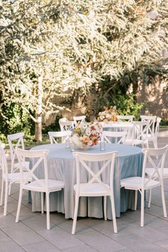 an outdoor table set up with white chairs and blue linens for a wedding reception