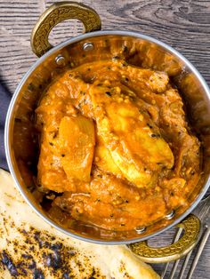 a pan filled with chicken curry next to some bread on top of a wooden table