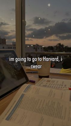 an open book sitting on top of a wooden table next to a laptop and pen