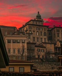 the sky is red and pink as it sets in front of some old buildings with rooftops