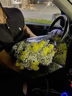 a woman sitting in the driver's seat of a car holding a bouquet of yellow and white flowers