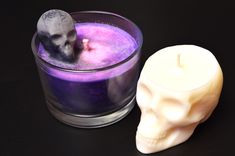 a candle with a skull on it next to a glass filled with purple and white liquid