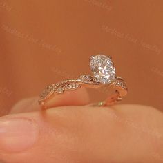 a woman's hand holding a ring with a diamond in the middle and an intricate band around it