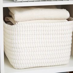 a white shelf with baskets and blankets on it