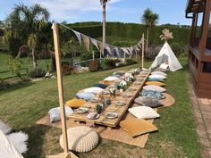 a long wooden table with many pillows and plates on it in the middle of a grassy area