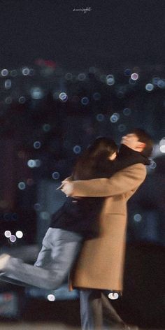 a man and woman are hugging in front of a cityscape at night with the lights of buildings behind them