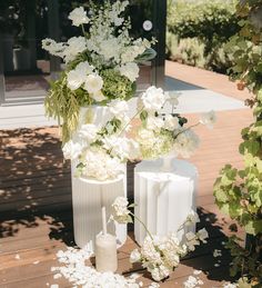 two white vases filled with flowers on top of a wooden floor next to each other