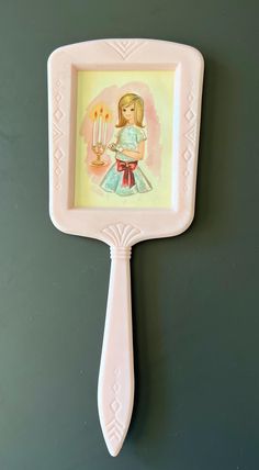 a pink toothbrush shaped like a girl with two candles in her hand on a green wall