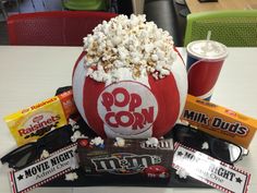 a popcorn bucket filled with lots of movies and snacks on top of a white table