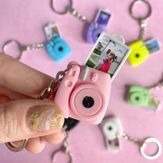 a hand holding a pink camera keychain with photos attached to the front and side