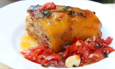 a white plate topped with meat covered in sauce and vegetables on top of a wooden table