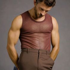 a man with his hands on his hips wearing brown pants and a tank top is looking down