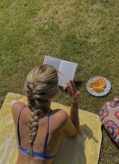 a woman sitting on top of a towel next to an open book and oranges