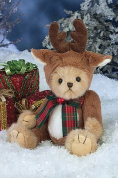 a teddy bear wearing a reindeer hat and scarf sitting in the snow next to presents