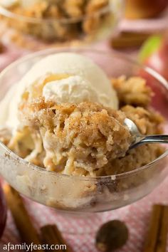 an ice cream sundae in a glass bowl with a spoon on the table next to apples