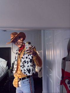 a man wearing a cow print shirt and hat taking a selfie in his bedroom