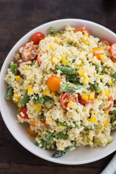 a white bowl filled with rice and vegetables on top of a wooden table next to a fork