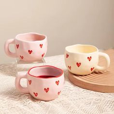 two mugs with hearts painted on them are sitting on a lace covered tablecloth