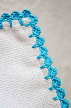 a close up of a blue crochet on a white cloth with an embroidered edge