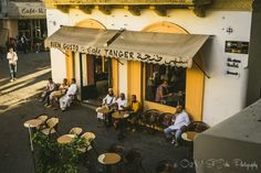 people are sitting at tables in front of a cafe