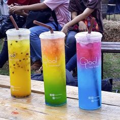 three different colored drinks sitting on top of a wooden table