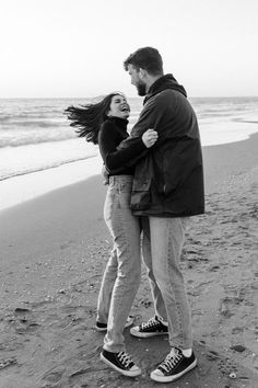 a man and woman standing on the beach with their arms around each other, smiling