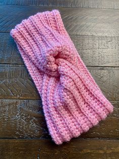 a pink knitted headband with a knot on top sitting on a wooden floor